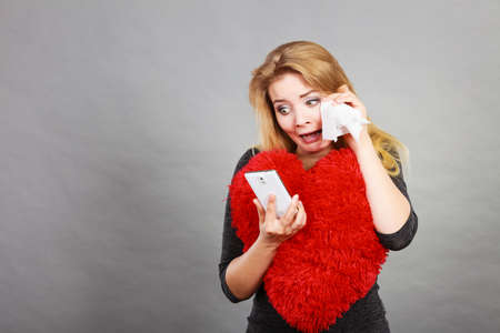 Betrayal, bad relationship, hurt love concept. Sad heartbroken woman crying and looking at her phone.の写真素材