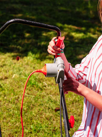 Gardening. Female person being mowing green lawn with lawnmower, in sunny day.の写真素材
