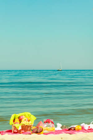 Relaxation during summertime concept. Picnic basket with fruit on red blanket near sea,の写真素材