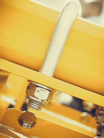 Construction machines concept. Detailed closeup of screw and bolts on yellow indrustrial machineryの写真素材