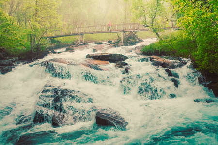 Travel and hiking. Tourist woman standing on bridge, enjoying waterfall torrential river along the Aurlandsfjellet mountains in Norway Sogn og Fjordane, foggy hazy summer dayの写真素材