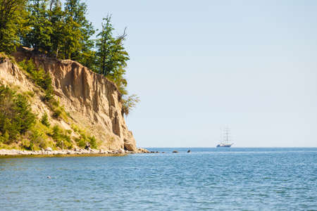 Beautiful landscape of high cliff with tress near sea and ship on blue water during summertime.の写真素材