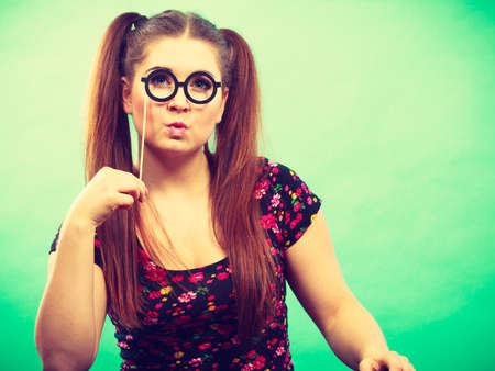 Happy young teenage woman holding fake eyeglasses on stick having fun. Photo and carnival funny accessories concept.の写真素材