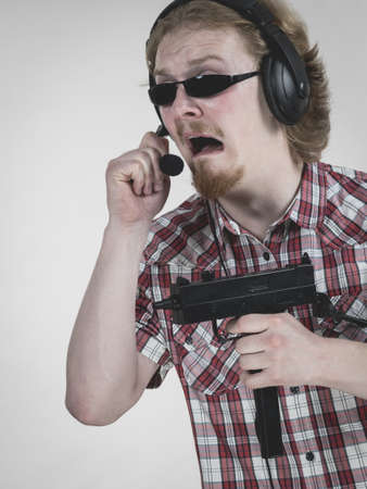 Nerd geek young adult man playing on the video console holding gun wearing headphones with...