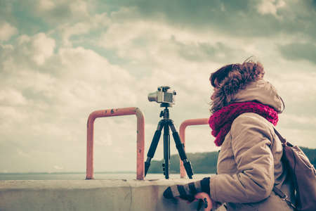 Woman having leisure time walking on coastline during autumnal weather taking pictures using cameraの写真素材
