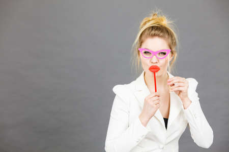 Happy elegant woman holding carnival accessoies on stick having fun at work wearing white office jacketの写真素材