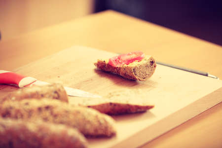 Bread sandwich with tomato slice on kitchen cutting board next to knife. Healthy breakfast concept.