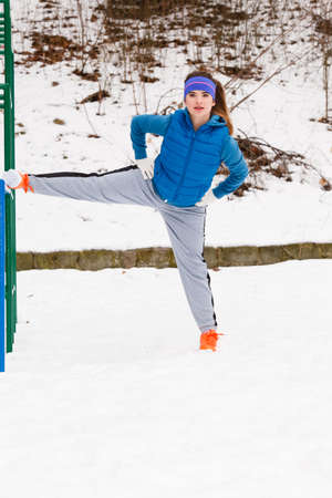 Outdoor sport exercises, sporty outfit ideas. Woman wearing warm sportswear training exercising stretching legs outside during winter.の写真素材