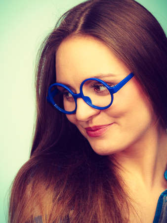 Studying, education and fun concept. Happy smiling nerdy woman in weird big glasses. Studio shot on blue backgroundの写真素材