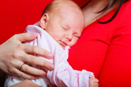 Family, childhood and parenthood concept. Little newborn baby sleeping on mother chest. Red backgroundの写真素材