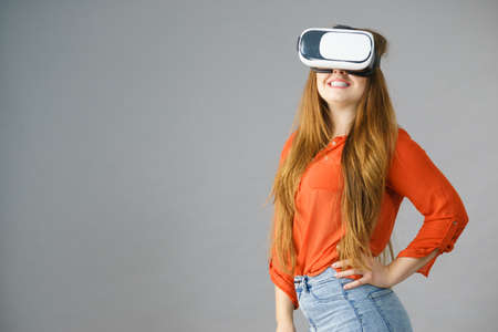Smiling positive woman wearing virtual reality goggles headset, vr box. Connection, technology, new generation and progress concept. Studio shot on grayの写真素材