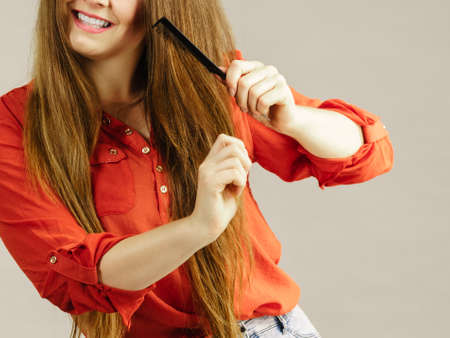 Happy funny teenage woman combing her long brown hair showing beautiful hairdo and non split ends.