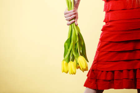 Unrecognizable confident woman wearing red dress holding yellow tulip bouquet. Women's day present concept.の写真素材