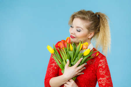 International women day, eight march. Beautiful portrait of pretty woman blonde hair with red yellow tulips, fashion make up, elegant outfit. Mother day. On blueの写真素材