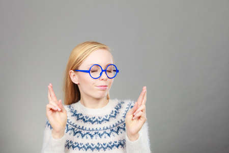 Gestures and signs concept. Teenage blonde woman making promise gesture with fingers crossed.の写真素材