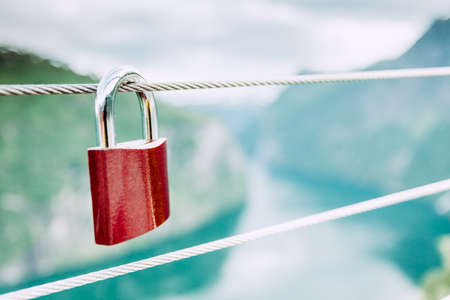 Tourism vacation and travel. Red love lock padlock on bridge and mountains, view over magical Geirangerfjorden from Flydalsjuvet viewpoint, Norway Scandinavia.の写真素材