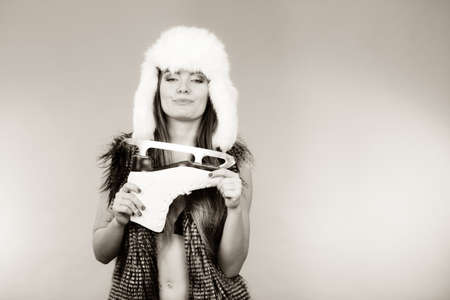 Winter sport activity concept. Woman wearing furry warm hat holding ice skate, blue background studio shot.の写真素材