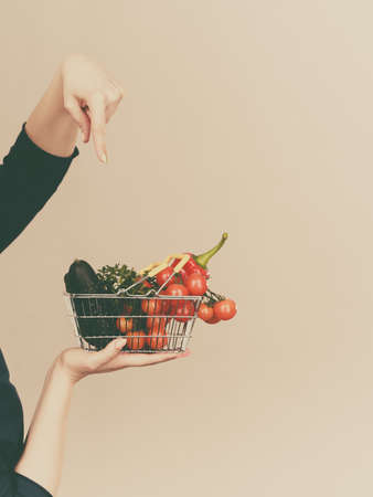 Lose weight, buying healthy food, vegetarian products. Hand holding shopping basket with vegetables, on greyの写真素材