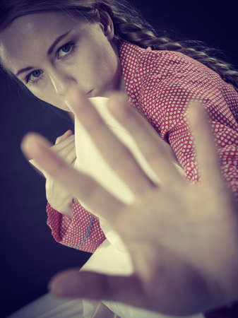 Adolescence problems concept. Sad young teenager woman sitting on bed feeling depressed hugging pillow and showing stop sign with palm handの写真素材