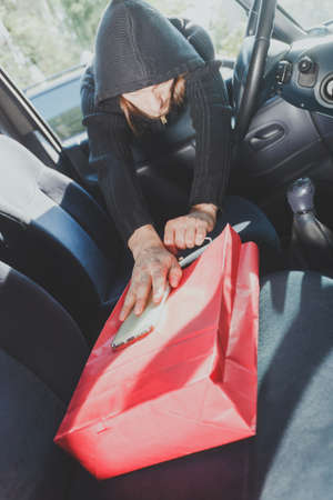 Anti theft system problem concept. Burglar thief man wearing black clothes breaking into car,...