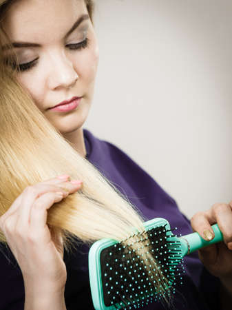 Woman combing her hair with brush. Young female with beautiful natural blond straight long hairs, studio shot on greyの写真素材