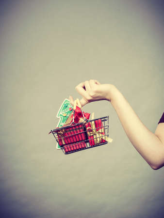 Xmas, seasonal sales, winter celebration concept. Woman hand holding shopping trolley cart basket with little christmas tree and gifts inside.の写真素材