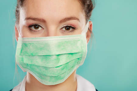 Close up of woman wearing medical face mask on teal backgroundの写真素材