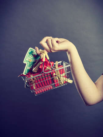 Xmas, seasonal sales, winter celebration concept. Woman hand holding shopping trolley cart basket with little christmas tree and gifts inside.の写真素材
