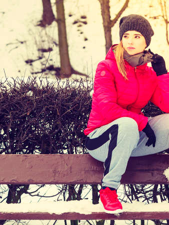 Outdoor sport exercising, sporty outfit ideas. Woman wearing warm sportswear relaxing after exercising sitting on bench outside during winter.の写真素材