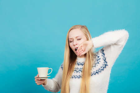 Addiction and caffeine need concept. Sleepy yawning blonde woman holding cup of coffee about to drink it.の写真素材