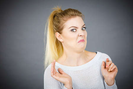 Disgusted young woman seeing something unpleasant having funny face expression, studio shot grey background.の写真素材