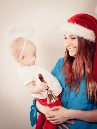 Christmas family holiday concept. Mother wearing santa claus hat holding and hugging baby in aureole.の写真素材