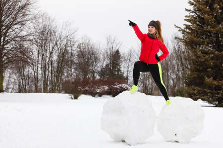 Outdoor sport exercises, sporty outfit ideas. Woman wearing warm sportswear training exercising outside during winter. Having fun while making snowmanの写真素材