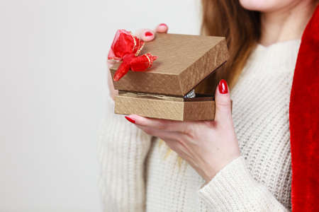 Woman hands red nails manicure opening golden gift box with jewel pearls. Christmas time, giving and...