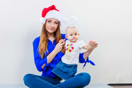 Family celebration concept. Christmas woman with cute baby. Beautiful lady has red santa claus cap.の写真素材