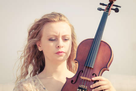 Music love, hobby and everyday passion concept. Woman on beach near sea holding violinの写真素材