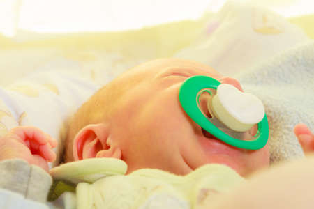 Infant care, beauty of childhood concept. Little newborn baby sleeping calmly in bed with teat in...