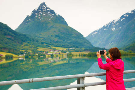 Tourism and travel. Woman tourist taking photo with camera, enjoying fjord mountains view, Sogn og Fjordane county. Norway Scandinavia.の写真素材
