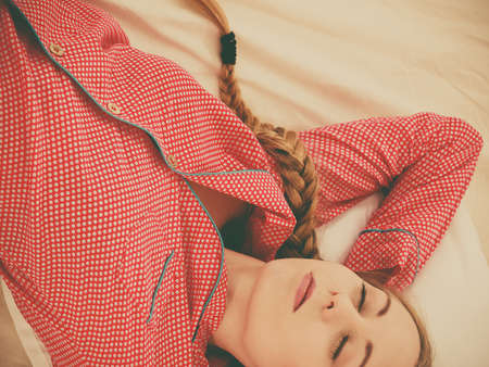 Relax rest sleep positions concept. Girl drowning in dreams. Young woman wearing red dotted pajamas lying in bed on back dreaming deeply.の写真素材