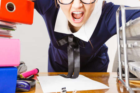 Mobbing at work, bad job relations concept. Angry mad bossy businesswoman being furious sitting working at desk full off documents in binders.の写真素材