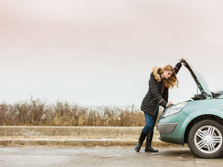 Accident and breakdowns with auto concept. Blonde woman and broken down car on road checking problem in engineの写真素材