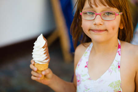 Summertime joy, summer recreation outside concept. Toddler girl in eyeglasses eating ice cream, having funの写真素材