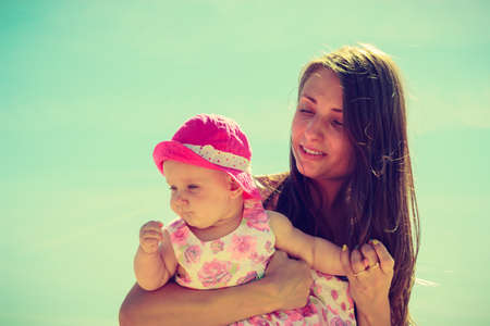 Woman holding child in swimsuit and hat on sunny dayの写真素材