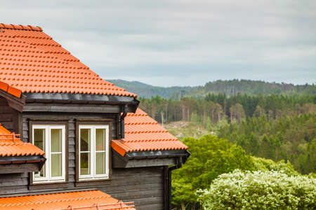 Place to live, beautiful view concept. Norway forest landscape, wooden house with red roof and windows in foreground.の写真素材