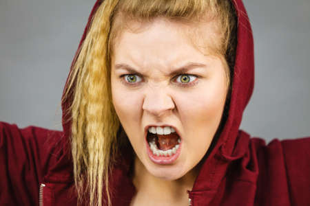 Angry energetic motivated blonde woman wearing sporty outfit, red hoodie. Female having screaming face expressionの写真素材