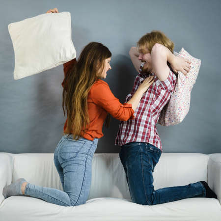 Happy funny siblings couple having pillow fight for fun. Enjoying leisure time with friends at home.の写真素材