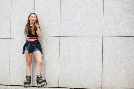 Young woman wearing roller skates standing against concrete wall in city. Female being sporty having fun during summer time.の写真素材