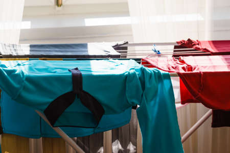 Many colorful clothes from laundry hanging on drying rack at home next to window.の写真素材