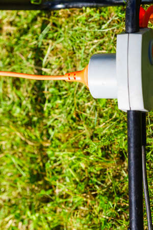 Electricity in garden. Electrical cord plug connected to power socket outdoor, grass background