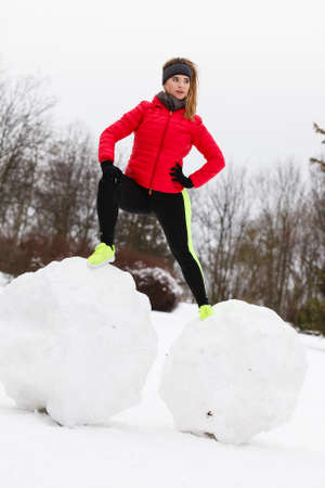 Outdoor sport exercises, sporty outfit ideas. Woman wearing warm sportswear training exercising outside during winter. Having fun while making snowmanの写真素材